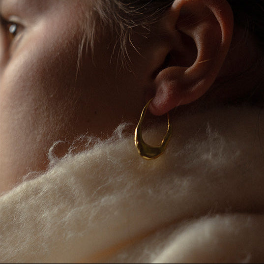 Close-up of a person wearing a gold hoop earring with a soft focus background.
